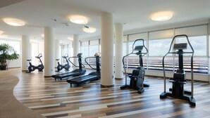A gym with treadmills, stationary bikes, and elliptical machines, large windows, and a patterned floor.