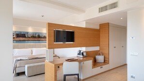Una habitación de hotel moderna con un escritorio de madera, una cama, un televisor y un cuadro de un paisaje.