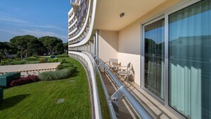A modern hotel balcony with a curved railing, a seating area, and a view of the surrounding greenery.