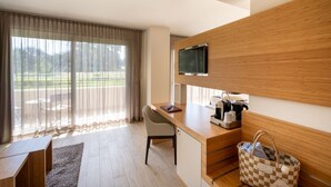 Una habitación de hotel moderna con un escritorio de madera, un televisor montado en la pared, una cafetera y un bolso cuadriculado en el suelo.