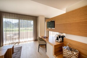 A modern hotel room with a wooden desk, a television mounted on the wall, a coffee maker, and a checkered bag on the floor.