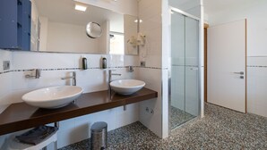 Ein modernes Badezimmer mit zwei Waschbecken, einem großen Spiegel und einer Duschkabine aus Glas.