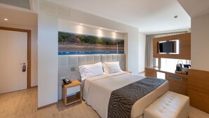 Ein modernes Hotelzimmer mit einem großen Bett, einem Nachttisch mit Telefon, einem Flachbildfernseher und Blick auf einen Strand durch ein Fenster.
