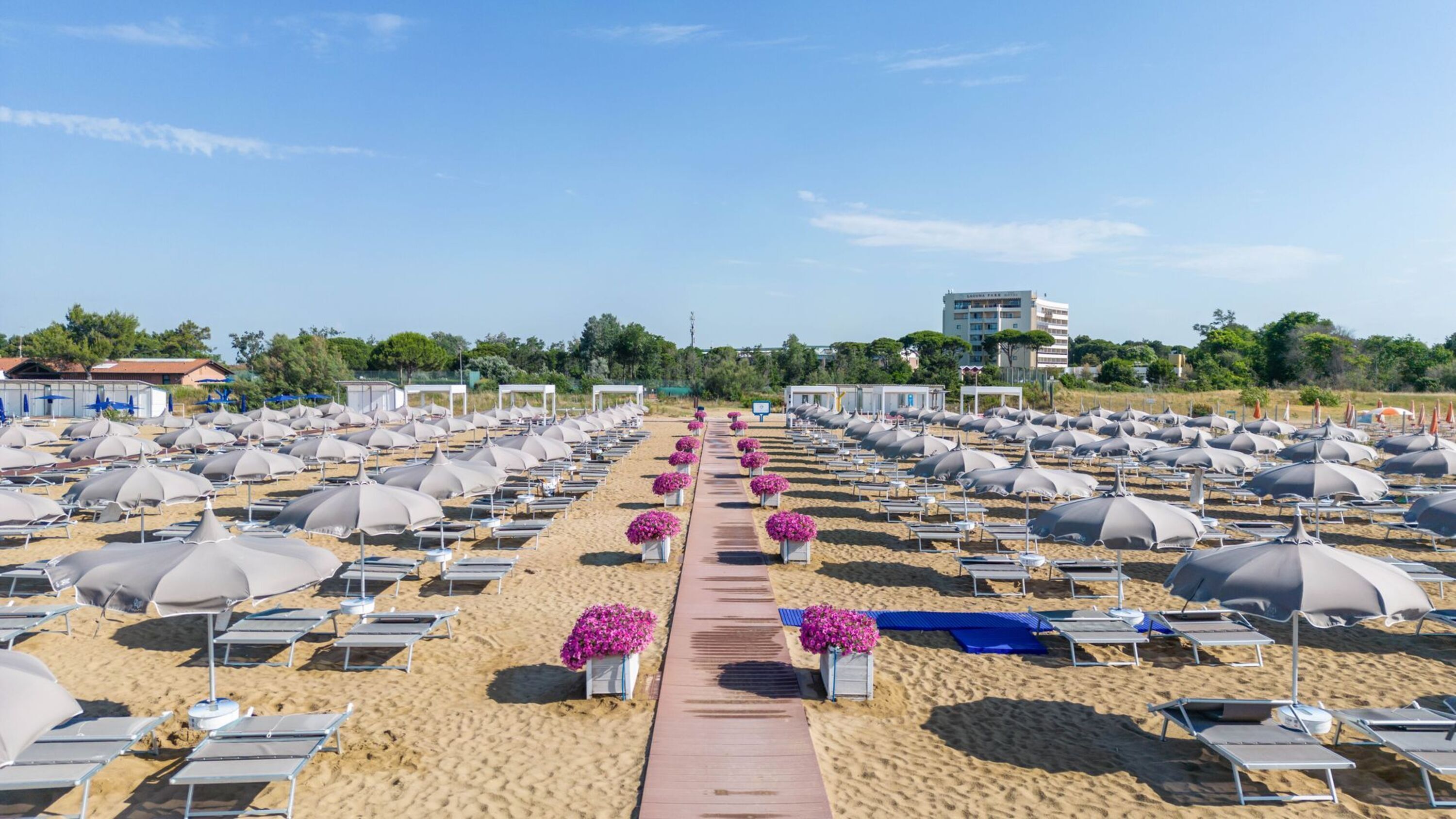 Une plage bordée de rangées de chaises longues et de parasols, une allée centrale et un bâtiment en arrière-plan.