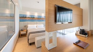 Une chambre d’hôtel moderne avec un grand lit, un téléviseur fixé sur un panneau en bois, un bureau avec un ordinateur portable et un tableau au mur.