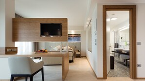 Un salon moderne comprenant un coin repas, un téléviseur fixé sur un panneau en bois, un canapé et une petite table sur laquelle sont disposés des fruits.