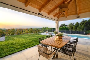 An outdoor patio with a wooden table and chairs, a pool, and a view of a green landscape. - Luxury Villa Sofia | Private Pool & Garage (Porec)