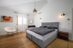 A modern bedroom with a grey bed, a white chair, and a large window with white curtains. - Luxury Villa Sofia | Private Pool & Garage (Porec)