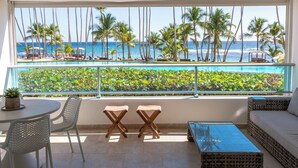 A balcony with a view of the ocean and palm trees, a round table with two chairs, and a wicker sofa.