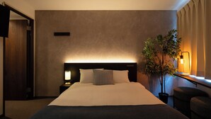 A hotel room with a large bed, a bedside table with a lamp, a potted plant, and a view of the outdoors.