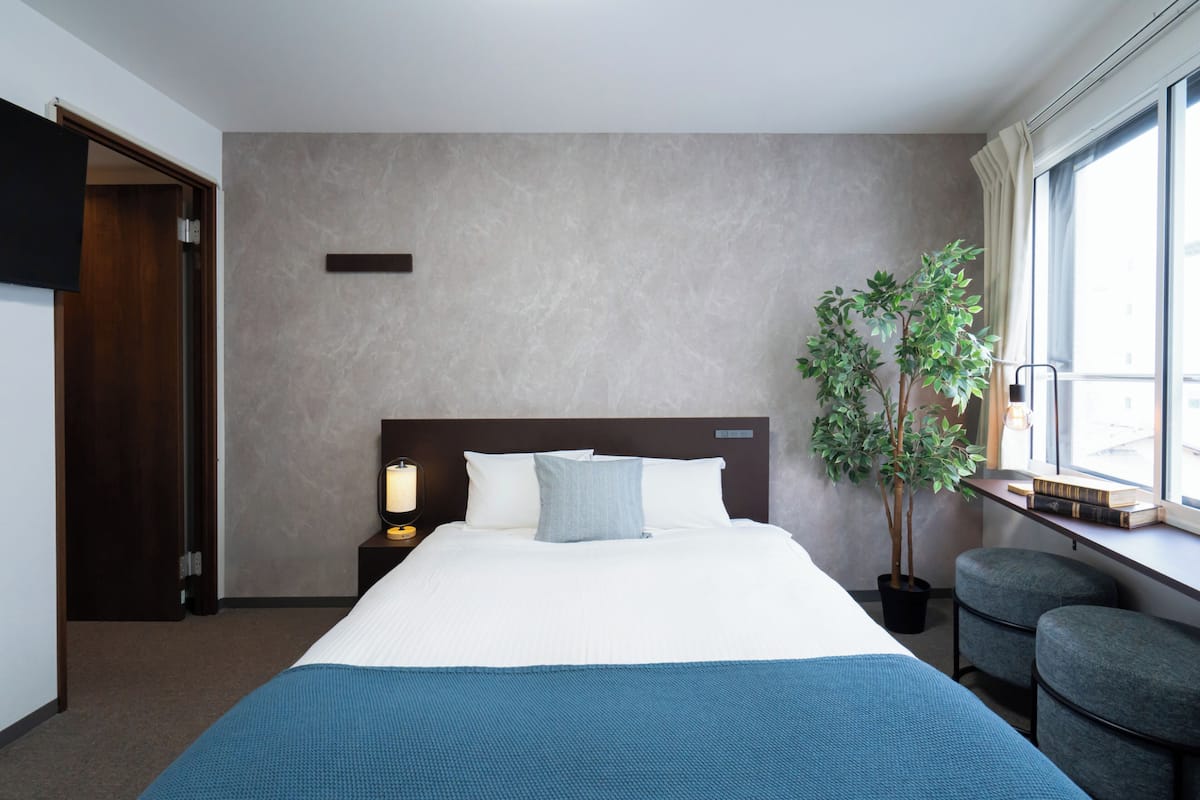 Ein Hotelzimmer mit einem großen Bett, einem Nachttisch mit Lampe, einer Topfpflanze und einem Fenster mit Aussicht.