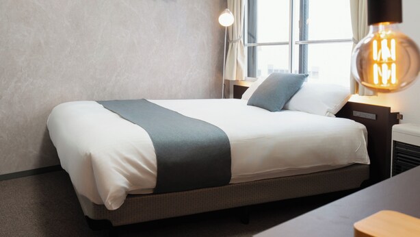 A neatly made bed with a grey and white duvet, a bedside lamp, and a wall-mounted heater.