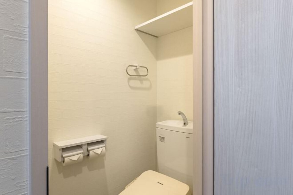 Un baño pequeño y cerrado con inodoro, lavamanos y dispensador de toallas.