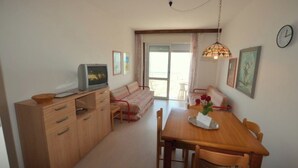 A compact living space with a kitchenette, a dining area, a sofa, and a television. - Seaside Bliss apartment with front sea view (Lignano Sabbiadoro)