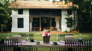 Un área de comedor al aire libre con una mesa dispuesta para una comida, un florero y un edificio al fondo.