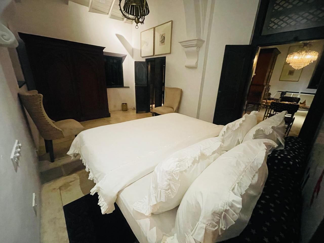 Una habitación de hotel con una cama grande, una silla, un escritorio y una araña.