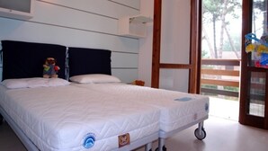 Un lit double avec un matelas sur roulettes, une petite étagère au-dessus du lit et une porte-fenêtre coulissante donnant sur un espace extérieur.