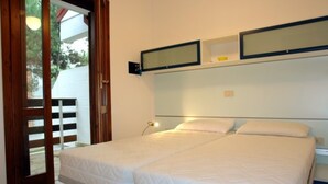A bedroom with two beds, a wooden door, and a small shelf with a mirror and a light. - Perfect holiday home with fenced garden in Lignano Pineta (Lignano Sabbiadoro)