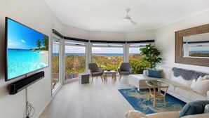 A modern living room with a large TV, comfortable seating, and a view of the ocean.