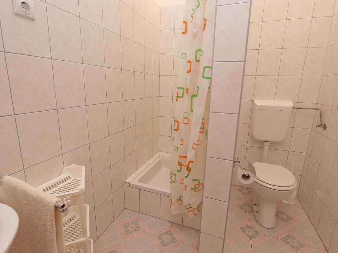 A small bathroom with a toilet, a shower with a patterned curtain, and a sink with a towel.