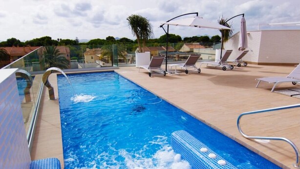 A rooftop swimming pool with clear blue water, lounge chairs, and umbrellas.