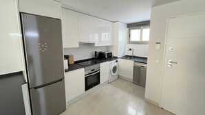 A compact kitchen with white cabinets, a stainless steel refrigerator, a built-in oven, a washing machine, and a dishwasher.