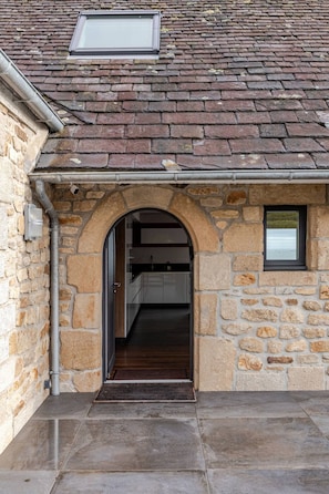 A stone building with a tiled roof, an archway entrance, and a small window.