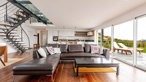 A modern living room with a sectional sofa, a coffee table, and a staircase with glass railings.