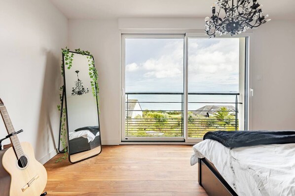 A bedroom with a bed, a guitar, a mirror with greenery, and a balcony with a view.