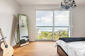 A bedroom with a bed, a guitar, a mirror with greenery, and a balcony with a view.