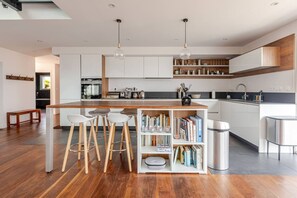 A modern kitchen with a central island, bar stools, and a bookshelf filled with books.