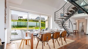 A dining area with a table set for six, a spiral staircase, and a view of a lake through large windows.