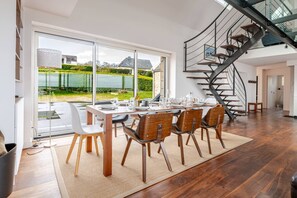 A dining area with a table set for six, a spiral staircase, and a view of a lake through large windows.