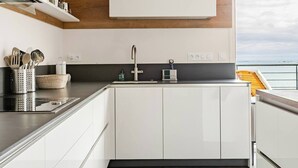 A modern kitchen with white cabinets, a wooden accent wall, a black countertop, and a view of the sea.