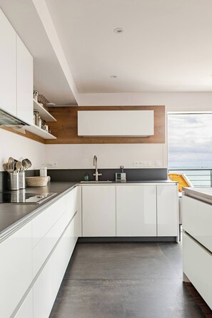 Une cuisine moderne avec des meubles blancs, un mur d’accent en bois et une vue sur la mer.
