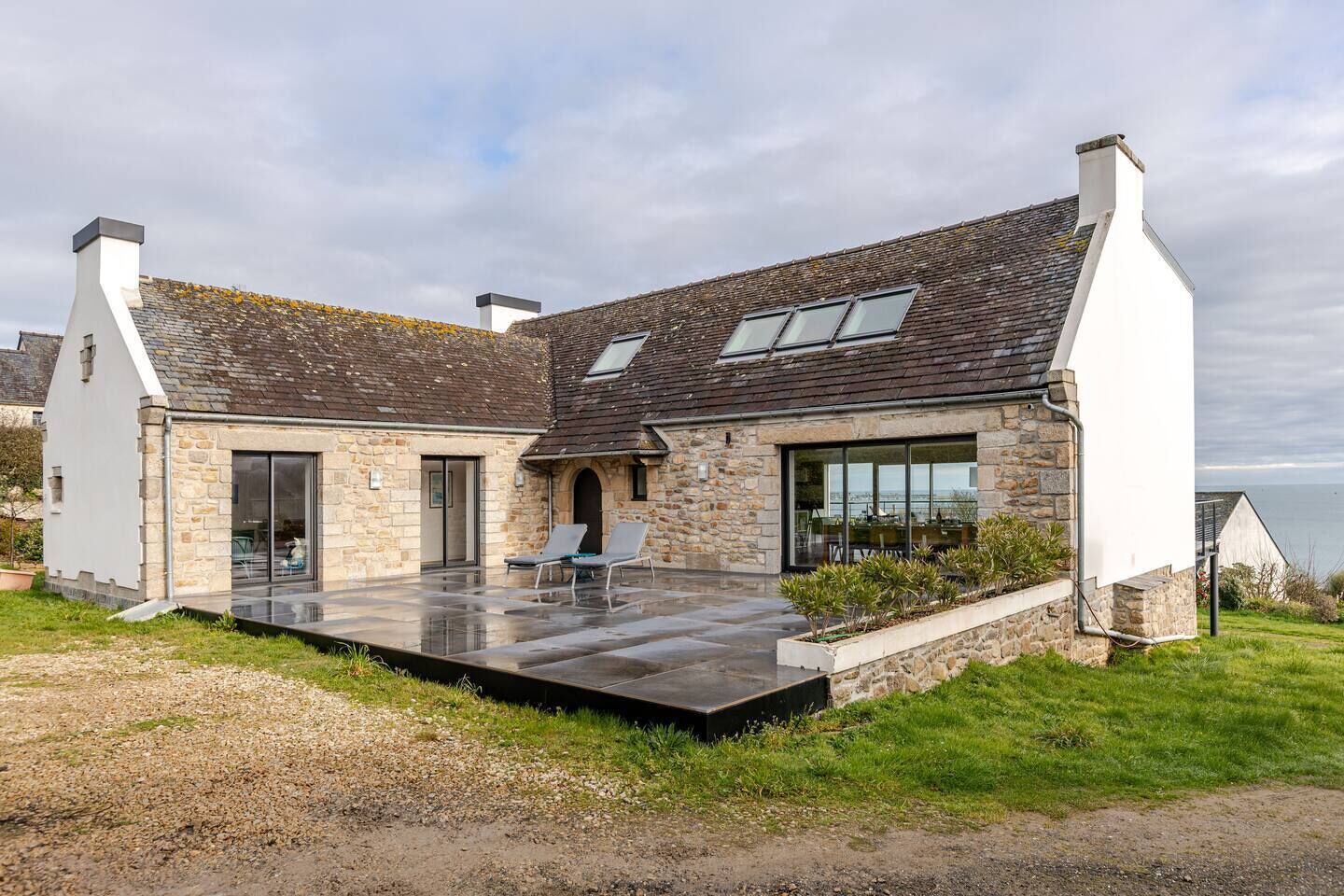 A modern house with a stone facade, large windows, and a patio with outdoor seating.