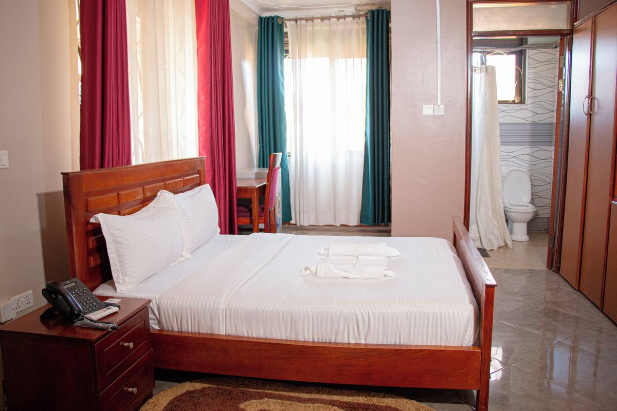 A neatly made bed with white linens, a wooden headboard, and a bedside table with a telephone.