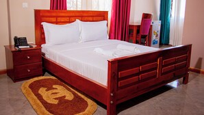 A neatly made bed with white linens, a wooden headboard, a bedside table with a phone, and a red and beige rug. - seed hotel  (Entebbe)