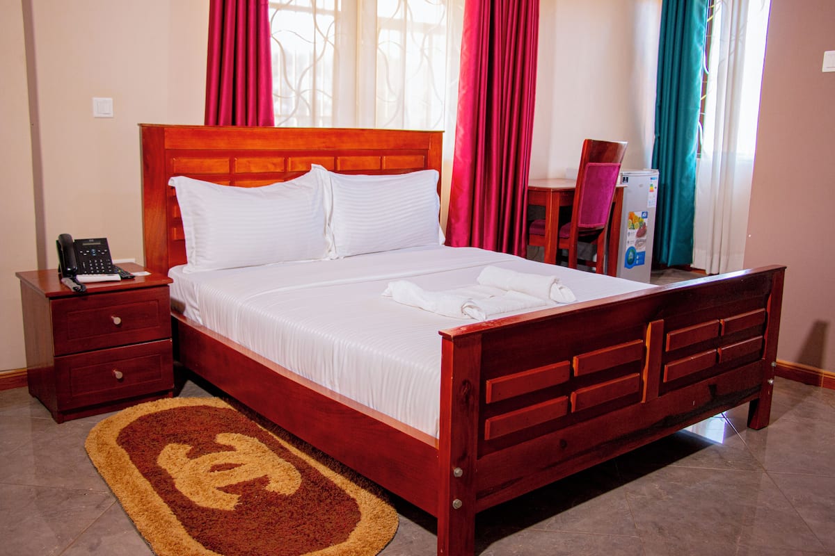 A neatly made bed with white linens, a wooden headboard, a bedside table with a phone, and a red and beige rug.