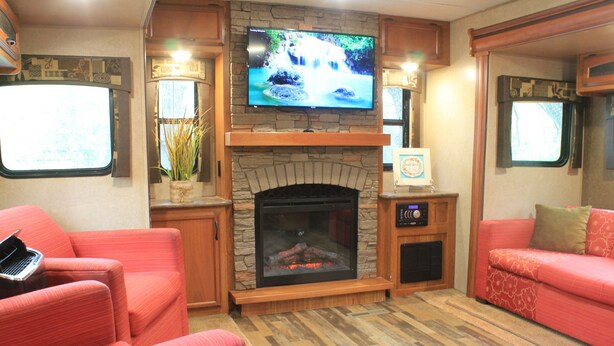 Een gezellig interieur van een camper, met een stenen openhaard, een flatscreen-tv erboven en twee rode banken.