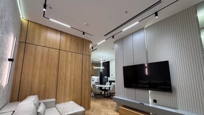 A modern living room with a sofa, a TV mounted on the wall, and a wooden panel wall. - NestOne SkyView (Тоshkent)