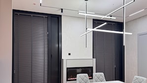 A modern dining area with a white marble table, grey upholstered chairs, a built-in fireplace, and contemporary lighting fixtures. - NestOne SkyView (Тоshkent)