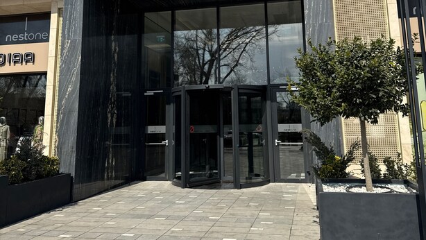 A Nestone building entrance with a marble facade, glass doors, and a small tree in the foreground. - NestOne SkyView (Тоshkent)