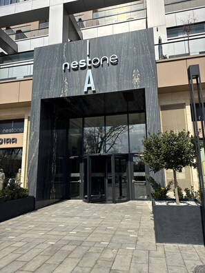 A Nestone building entrance with a marble facade, glass doors, and a small tree in the foreground. - NestOne SkyView (Тоshkent)
