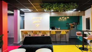 A modern office space with a black sofa, yellow chairs, a neon sign, and a kitchen area. - URBAN HUB PRESTON! Modern Studio Apartment - Located next to the UCLan campus (Preston)