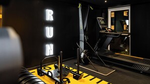 A gym with a treadmill, weights, and a wall with 'RUN' illuminated letters. - URBAN HUB PRESTON! Modern Studio Apartment - Located next to the UCLan campus (Preston)