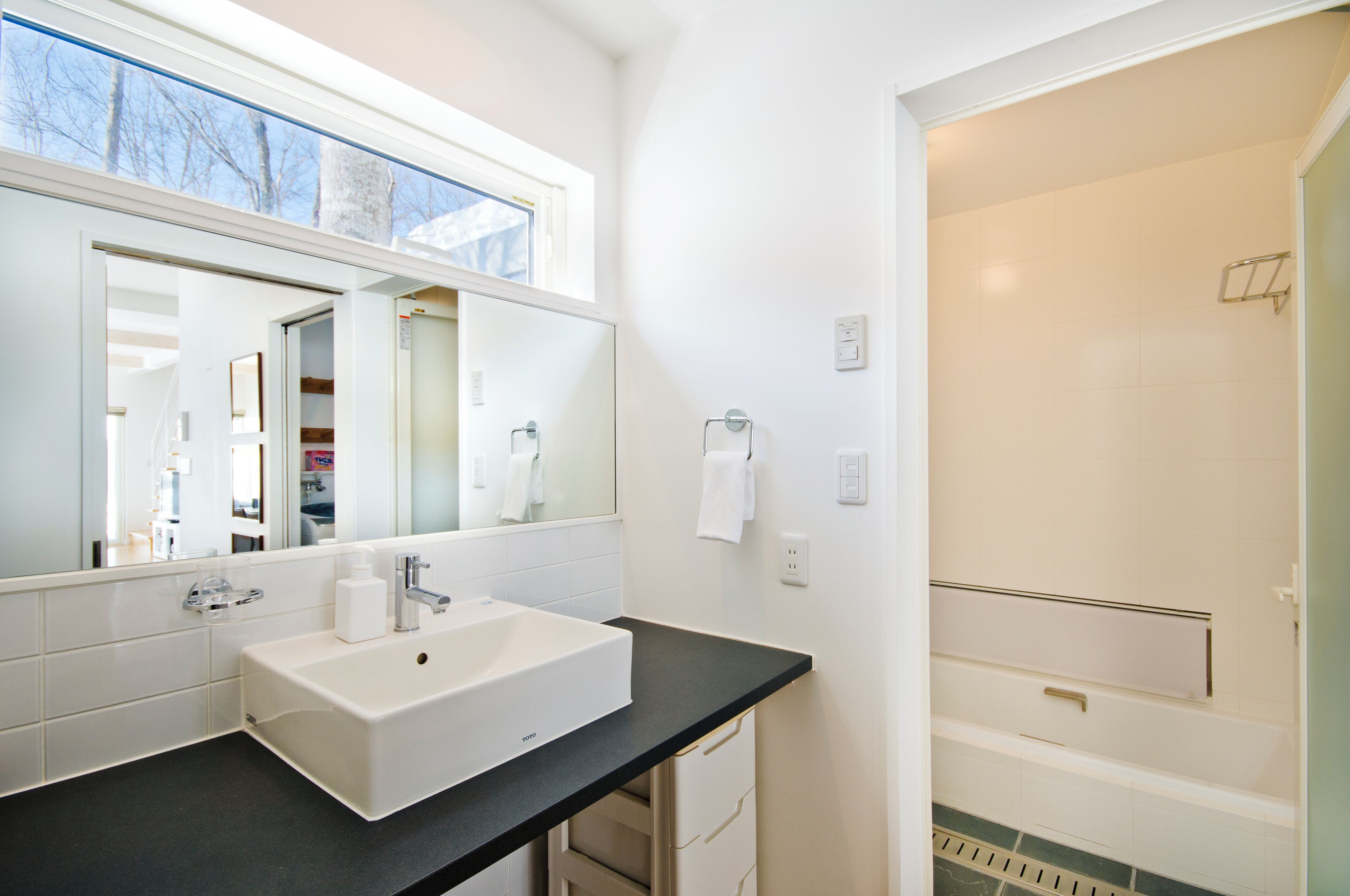 A modern bathroom with a large mirror, white sink, and a shower area.