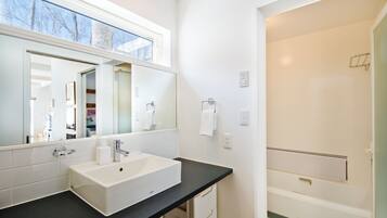 A modern bathroom with a large mirror, white sink, and a shower area.
