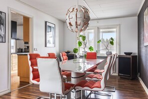 Un comedor moderno con una mesa de cristal, sillas blancas y rojas, y una lámpara colgante esférica original.