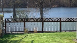 A fenced yard with a grassy area and a body of water in the background. - Ronneby Torneryd Retreat (Ronneby)